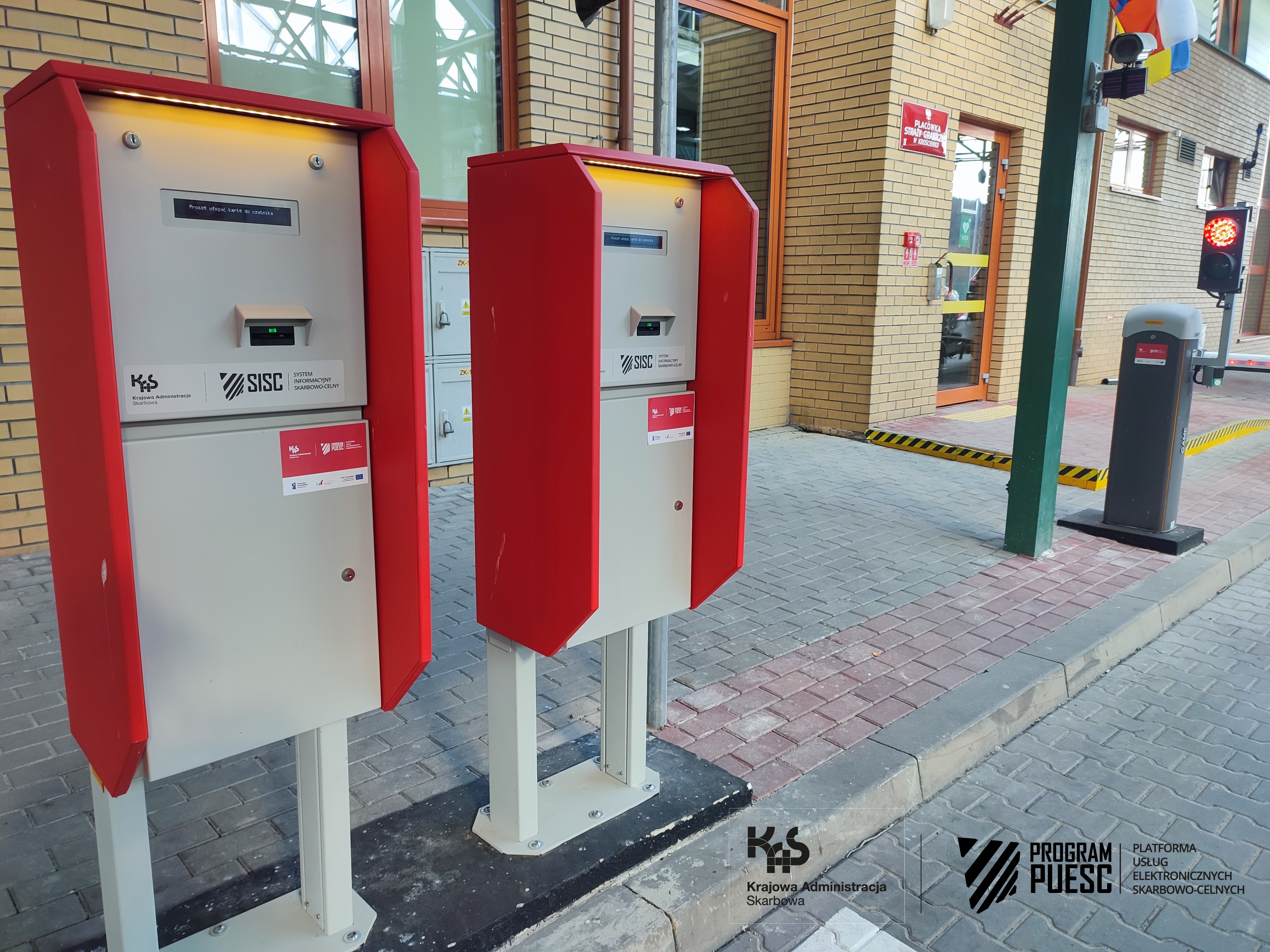 Devices located outside the border crossing point, supported on two supports. On the right side of the device there is a slot for inserting identification cards. The device has the following logos: National Revenue Administration, European Funds Digital Poland, Tax and Customs Information System, Ministry of Finance, European Union European Regional Development Fund.